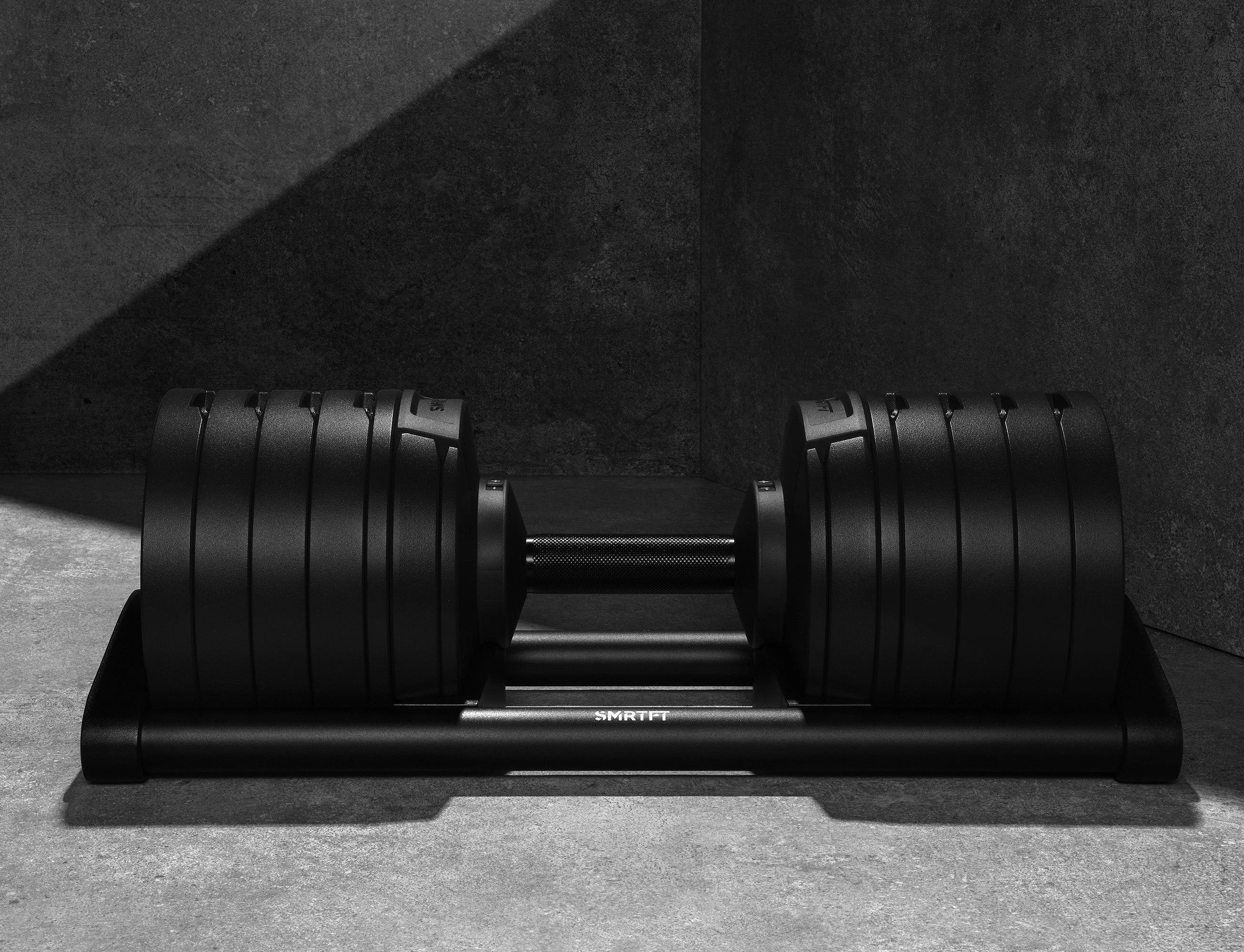 Current exact Matte Black SMRTFT NÜOBELL 100 manufacturer studio product image, showing one dumbbell in its selection cradle. The assessed package supplies two; a stand is separate.